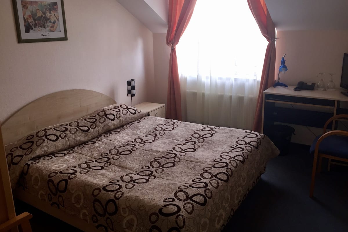 Ein Schlafzimmer mit Bett, Schreibtisch, Stuhl, Nachttisch, Lampe und einem gerahmten Bild an der Wand.