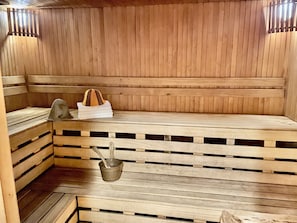 Una sauna con bancos de madera, un cubo de metal y un perchero para toallas.