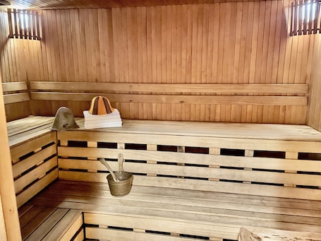 A sauna with wooden benches, a metal bucket, and a towel rack.