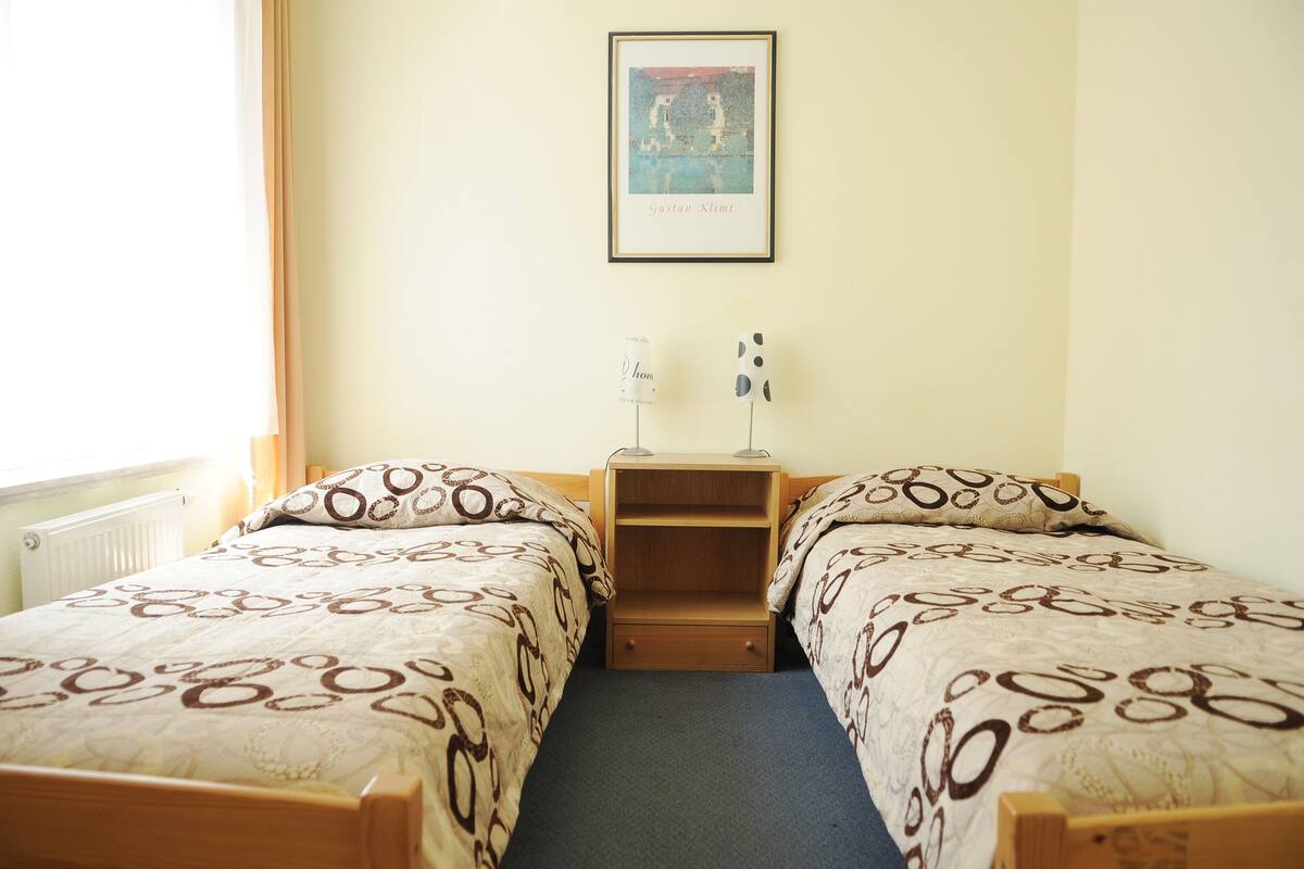 Ein Zimmer mit zwei Betten, einem gerahmten Bild an der Wand und einer kleinen Regaleinheit.
