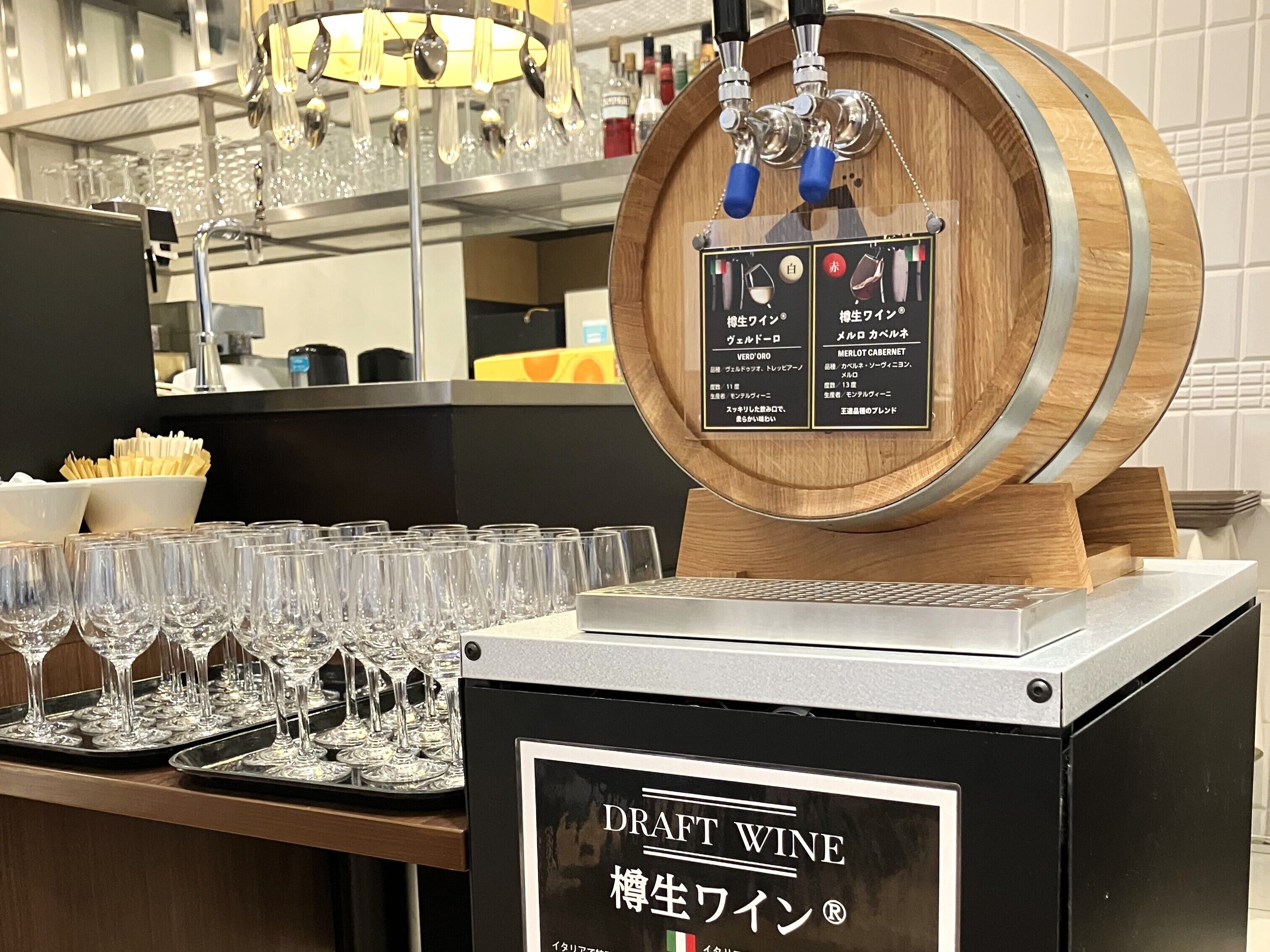 Un distributeur de vin composé d’un tonneau en bois, de verres et d’un panneau affichant la carte des vins.