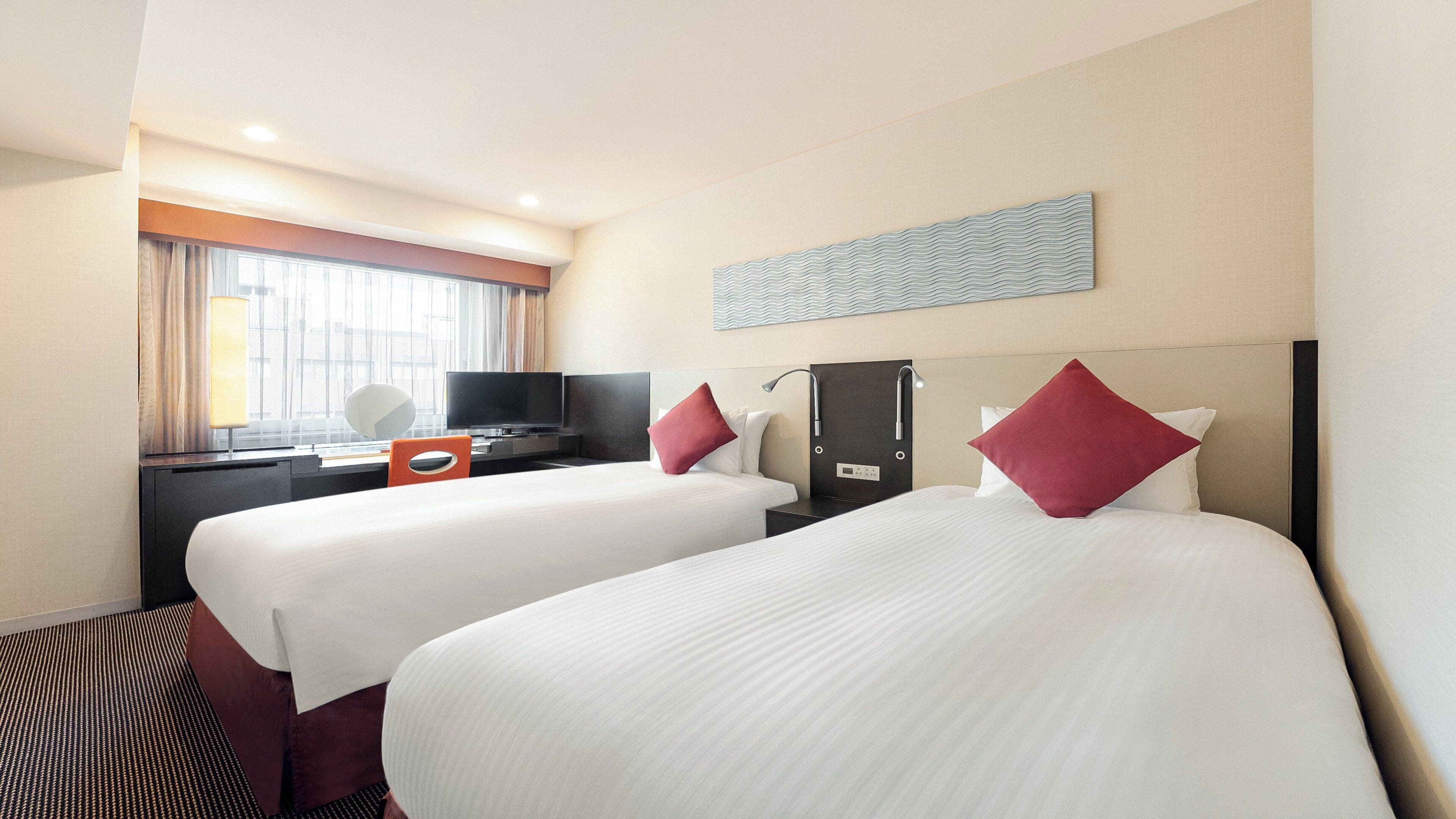A hotel room with two beds, a desk with a computer, a TV, and a window with curtains.