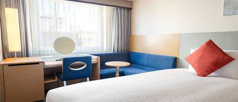 A hotel room with a bed, a desk, a chair, a small round table, and a large window with curtains.