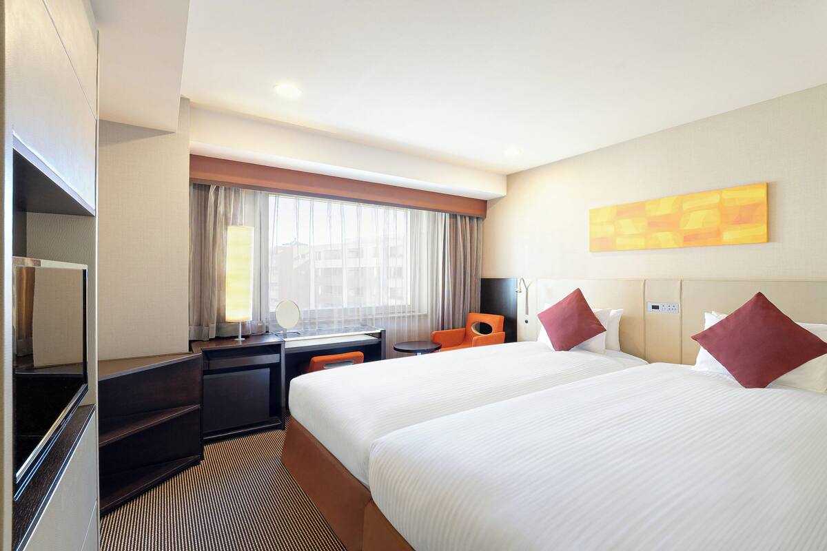 A hotel room with two beds, a desk, a chair, a TV, and a shower.