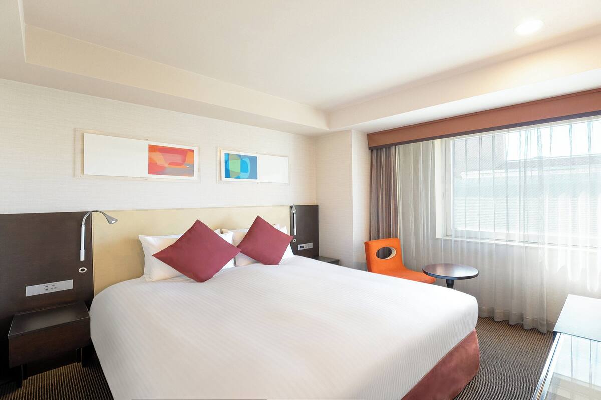 A hotel room with a large bed, a desk, a chair, and a window with curtains.