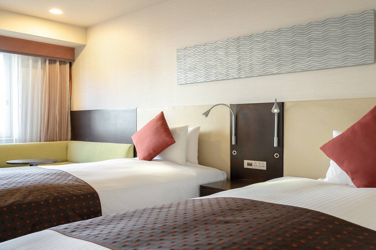 A hotel room with two beds, a sofa, a table, and a shower area.