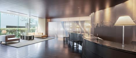 A modern interior with a curved reception desk, seating area, and large windows offering views of greenery.