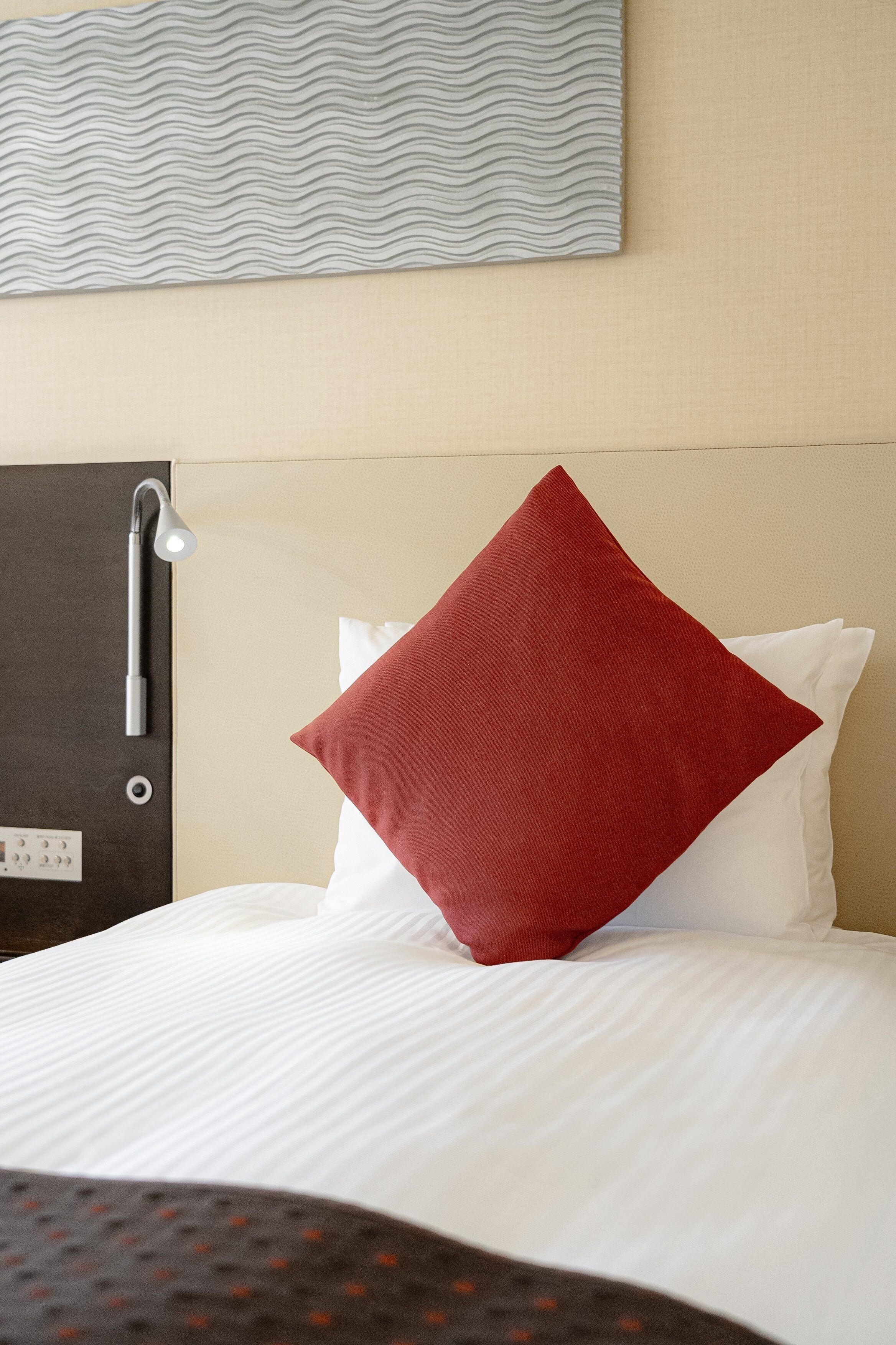 A neatly made bed with white bedding and a single red pillow.