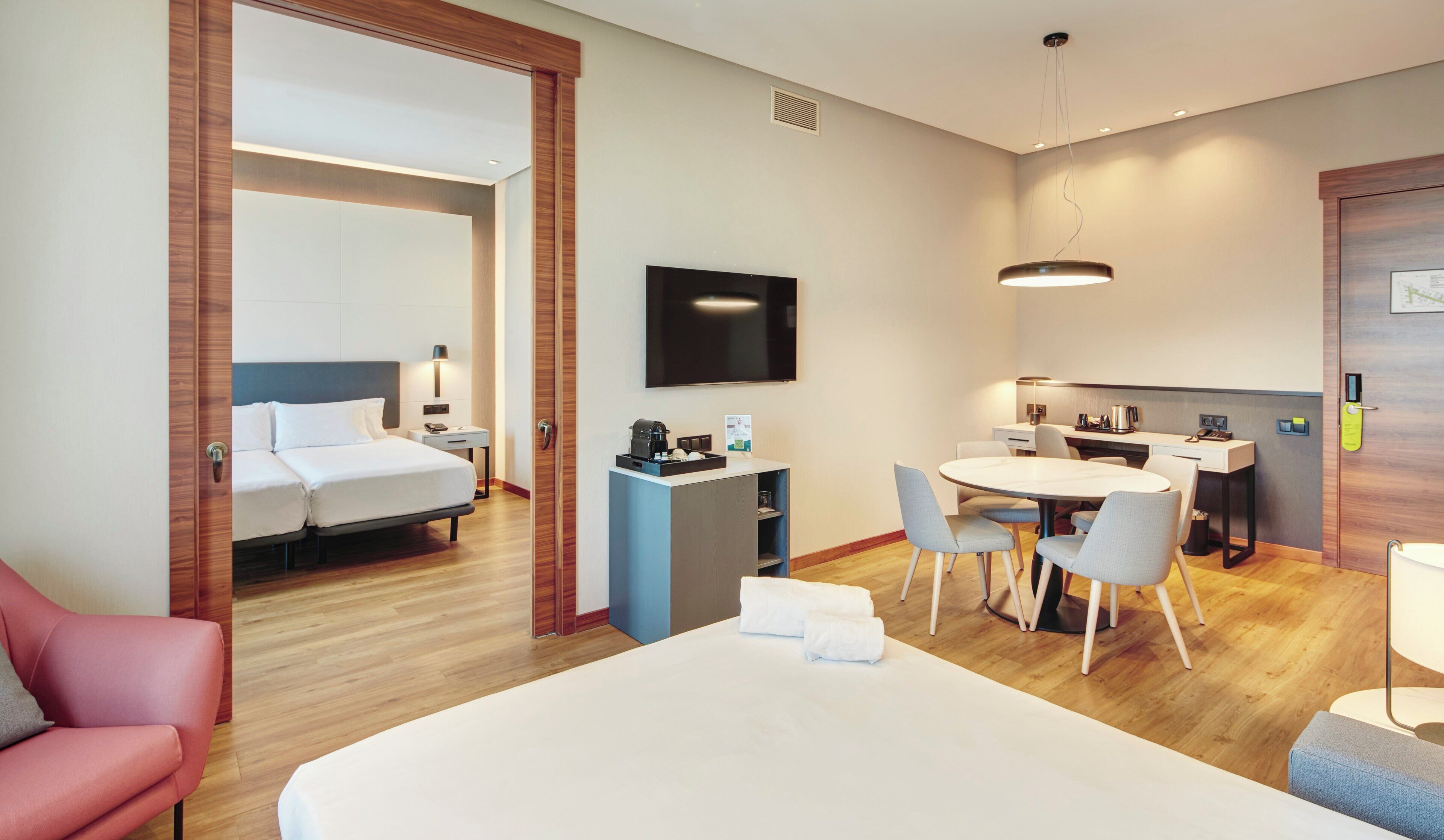 A hotel room with a bed, a desk, a chair, a TV, and a coffee machine.