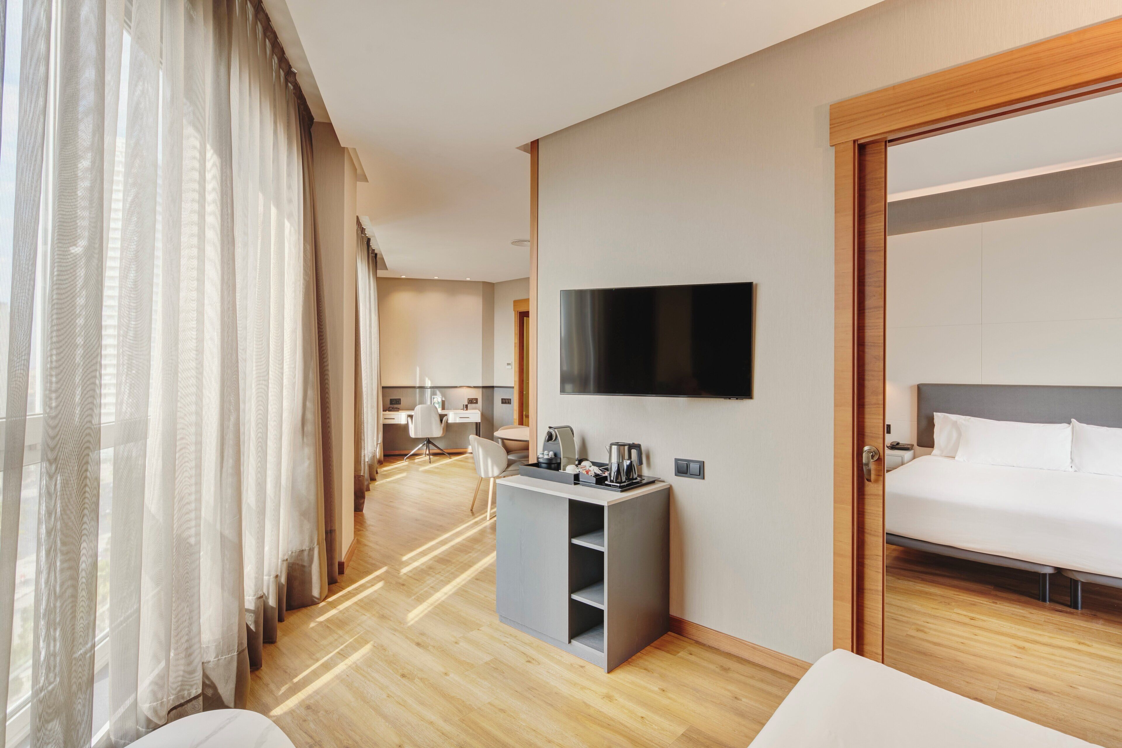 Une chambre d’hôtel avec un lit, un téléviseur fixé au mur, un bureau avec une chaise et une fenêtre avec des rideaux.