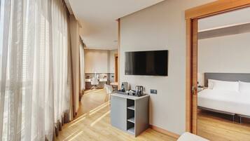 Une chambre d’hôtel avec un lit, un téléviseur fixé au mur, un bureau avec une chaise et une fenêtre avec des rideaux.