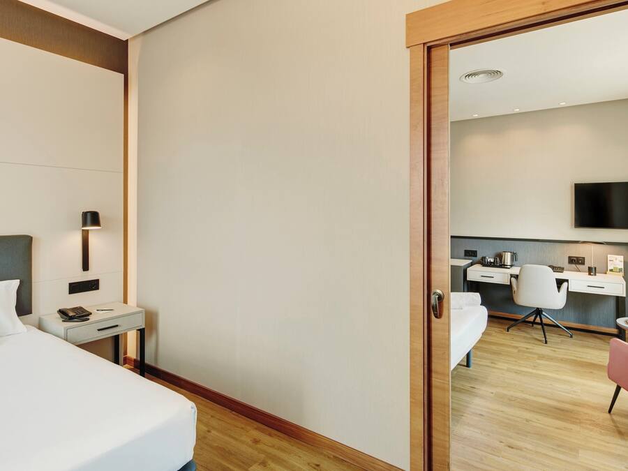 Una habitación de hotel con cama, mesita de noche, lámpara y escritorio con silla y televisión.