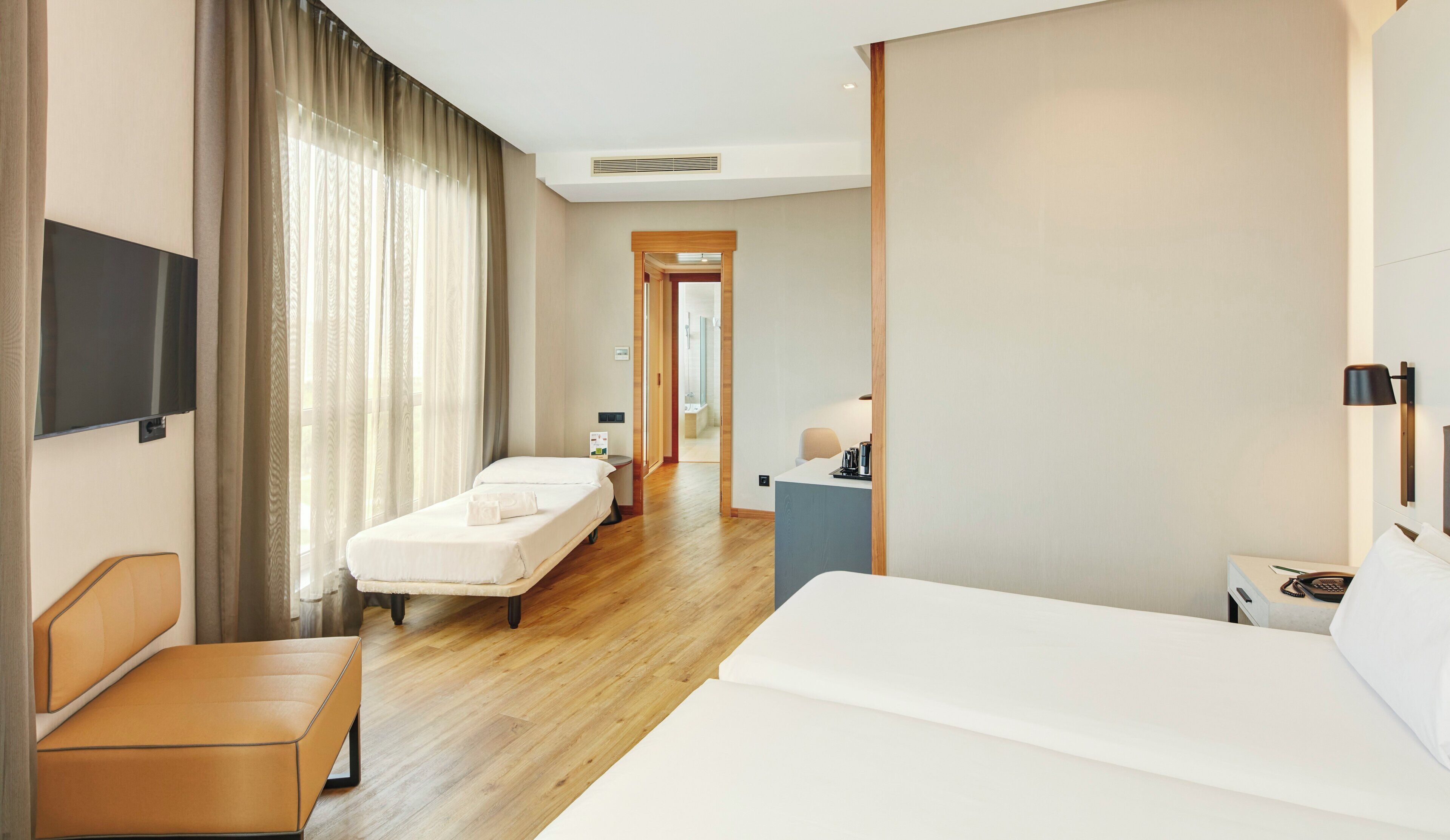 A hotel room with a bed, a bedside table, a chair, a desk, a TV, and a bathroom visible through an open door.