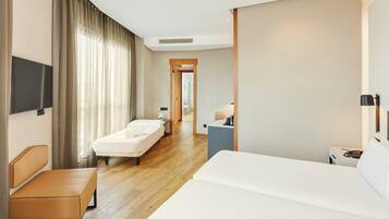 A hotel room with a bed, a bedside table, a chair, a desk, a TV, and a bathroom visible through an open door.