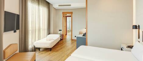 A hotel room with a bed, a bedside table, a chair, a desk, a TV, and a bathroom visible through an open door.