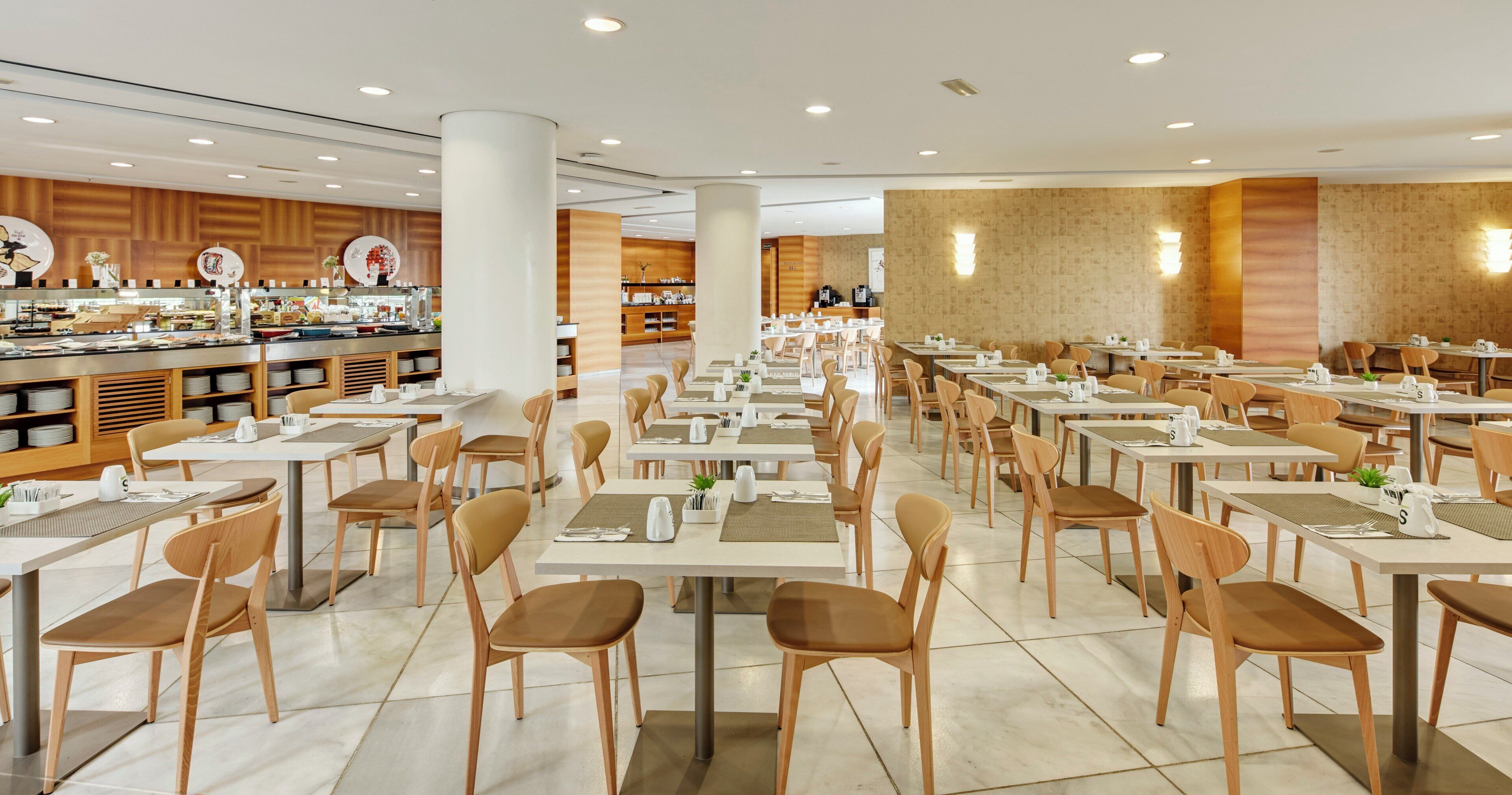 Un amplio comedor con varias mesas y sillas, una barra de buffet y un mostrador con diferentes opciones de comida.
