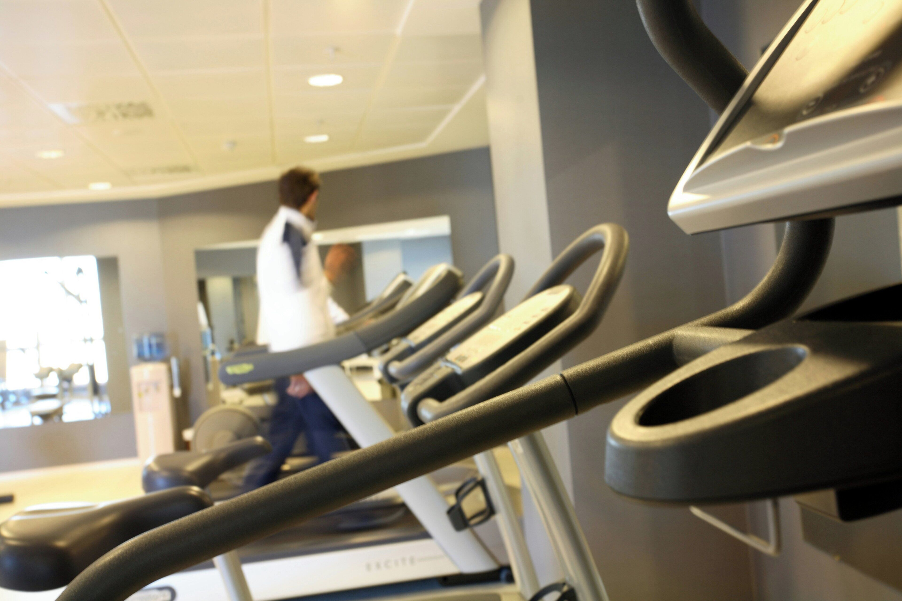 Un gimnasio con cintas de correr, una persona caminando en una cinta y un televisor montado en la pared.
