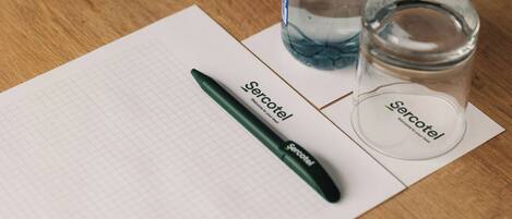 A grid notebook, a pen, a glass of water, and a glass jar on a wooden surface.
