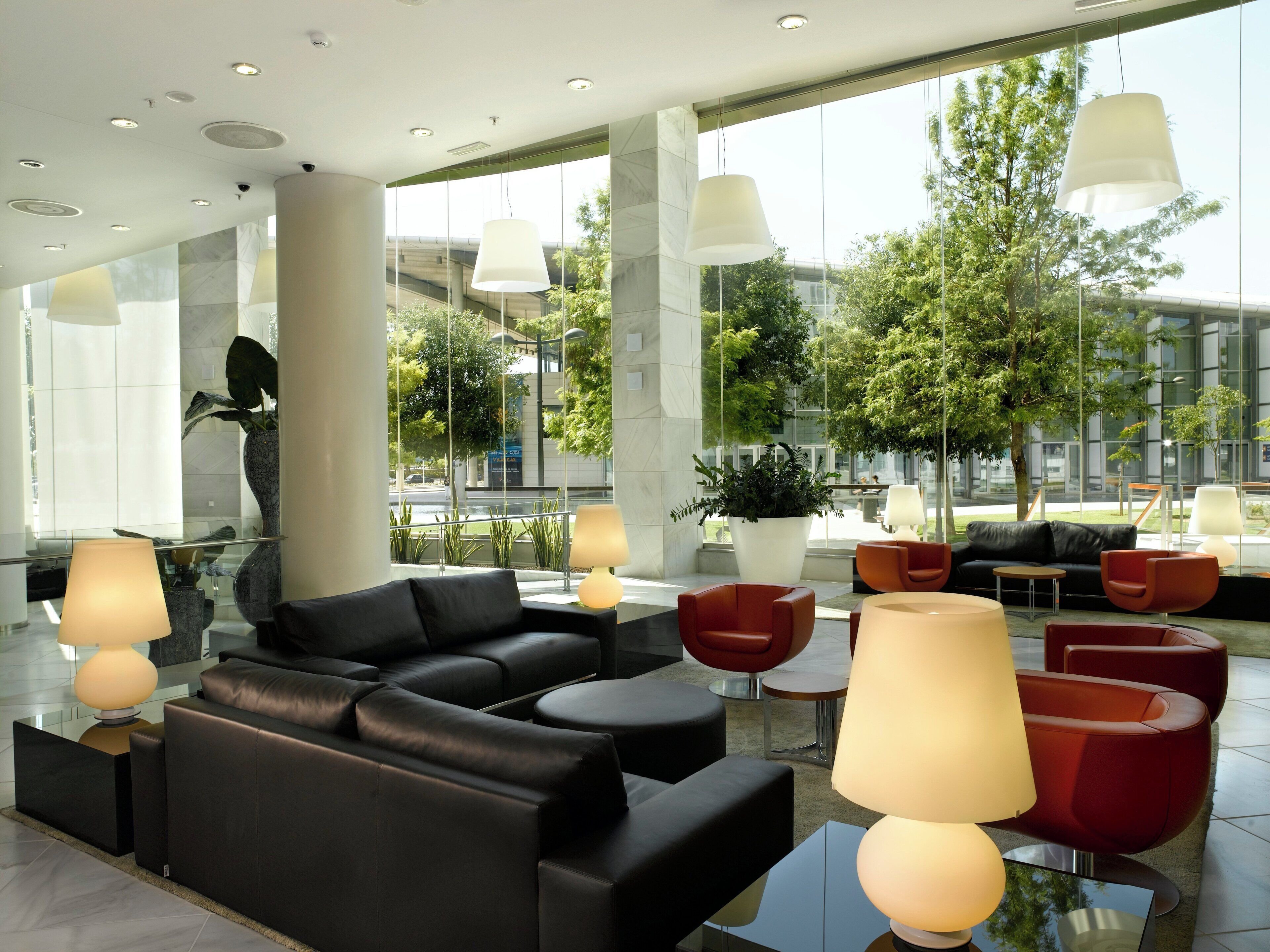 Un hall d’entrée moderne avec des canapés en cuir, des fauteuils rouges et de grandes fenêtres donnant sur l’extérieur.
