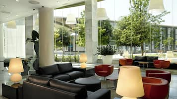 Un hall d’entrée moderne avec des canapés en cuir, des fauteuils rouges et de grandes fenêtres donnant sur l’extérieur.