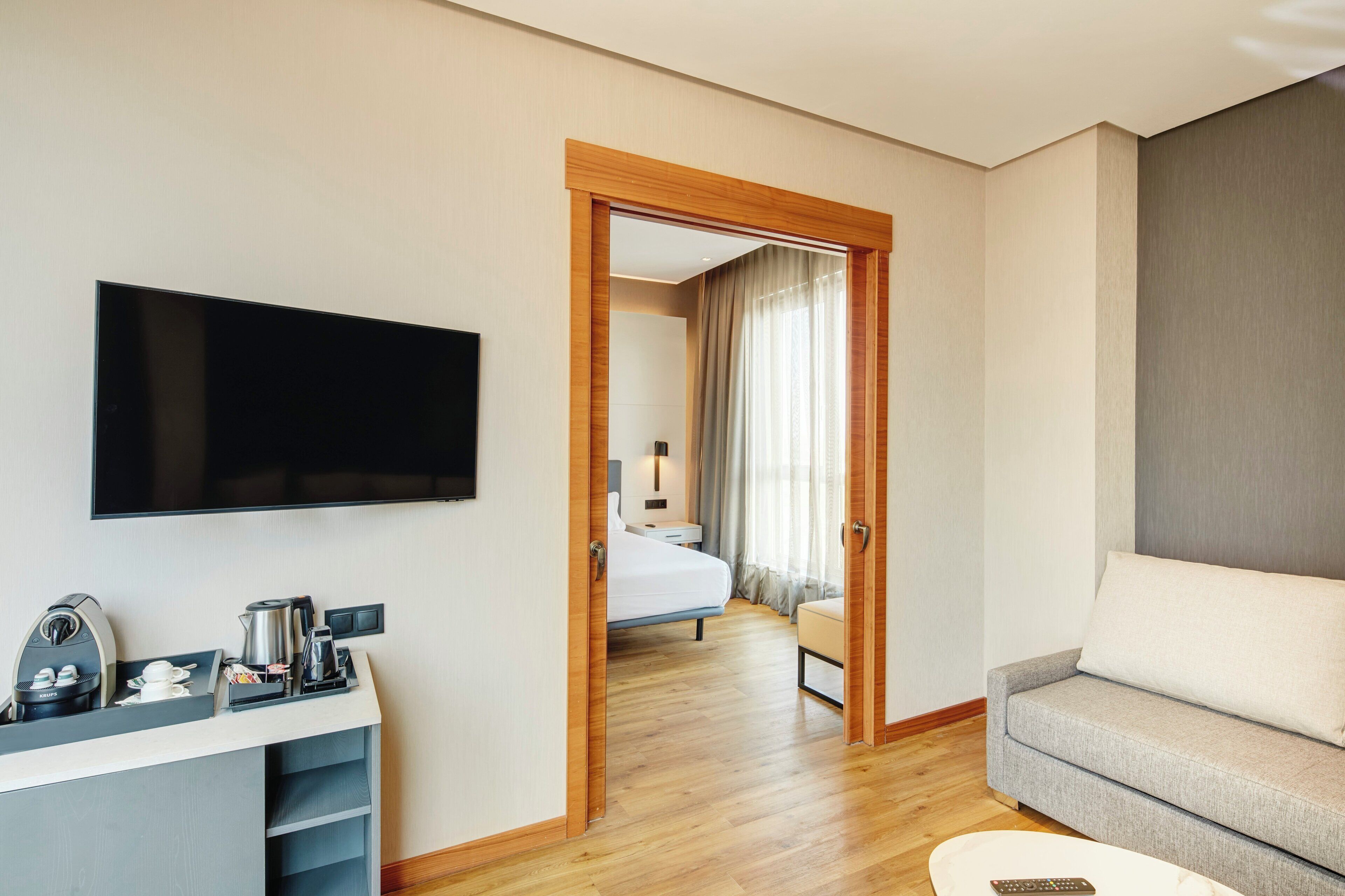Habitación de hotel con televisor de pantalla plana, cafetera, sofá y cama con vistas a un balcón.
