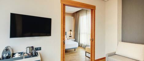 A hotel room with a flat-screen TV, a coffee machine, a sofa, and a bed with a view of a balcony.