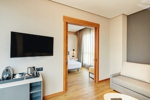Habitación de hotel con televisor de pantalla plana, cafetera, sofá y cama con vistas a un balcón.