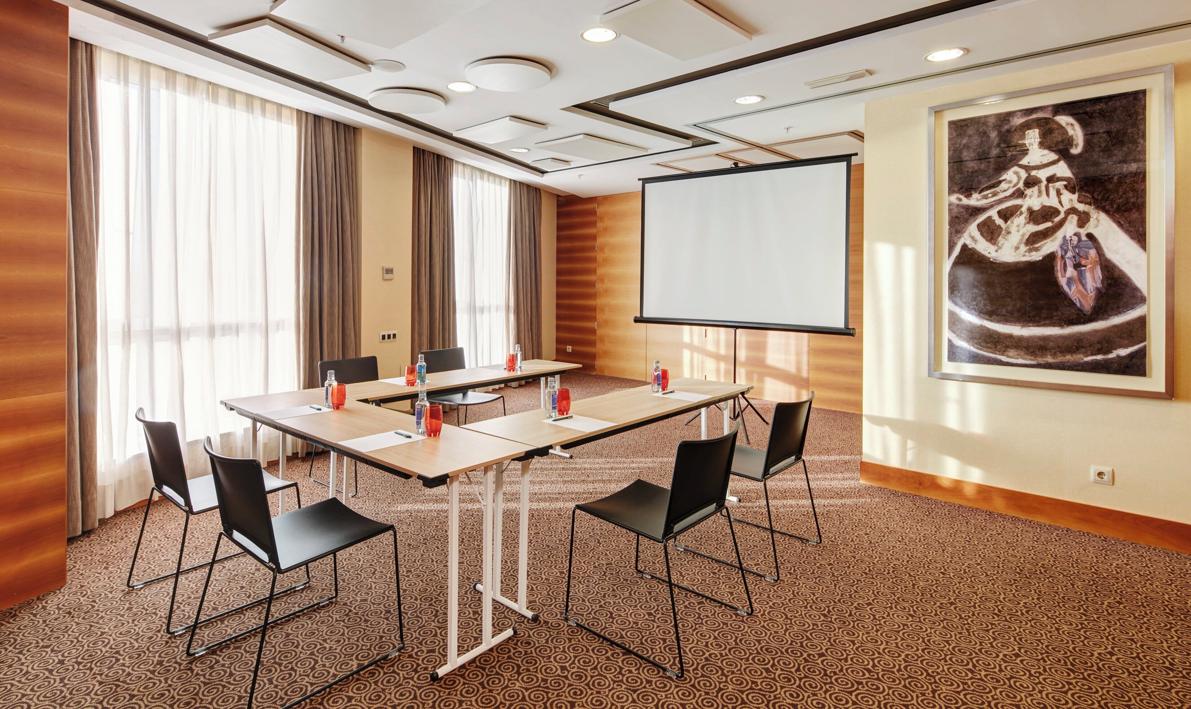 A conference room with a large table, chairs, a projector screen, and a painting on the wall.