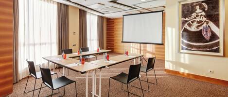A conference room with a large table, chairs, a projector screen, and a painting on the wall.