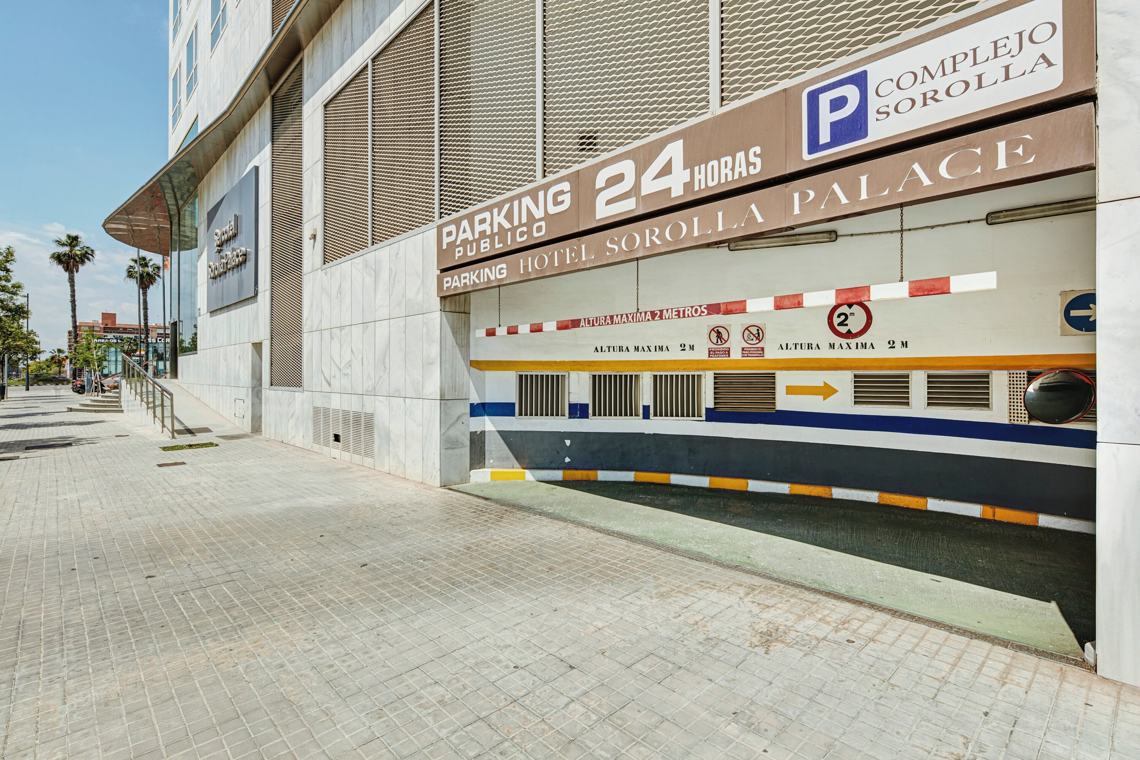 Entrada de hotel con un cartel que indica estacionamiento las 24 horas, un límite de altura de 2 metros y una flecha direccional.