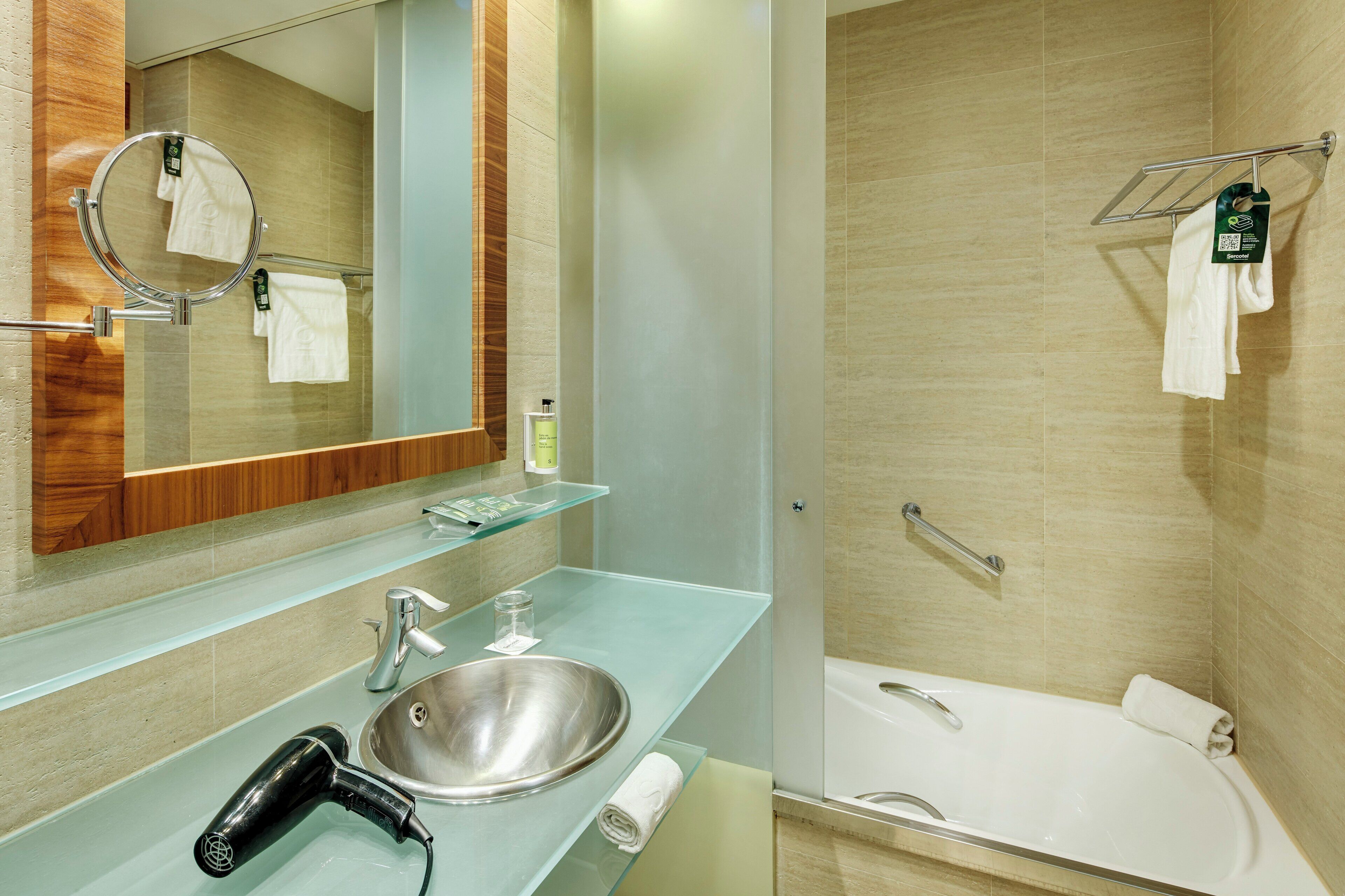Een moderne badkamer met een glazen wastafel, een ronde spiegel, een handdouche en een bad.