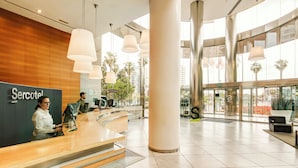 A hotel reception area with a modern design, featuring a reception desk, large columns, and a view of palm trees through the windows. - Sercotel Sorolla Palace Hotel (Valencia)
