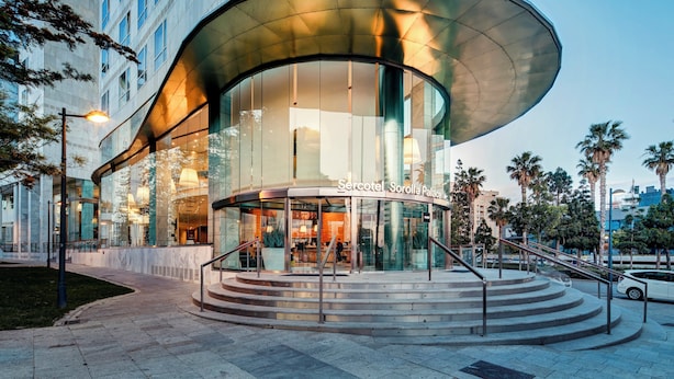 A modern hotel with a curved glass facade, a central staircase, and a sign reading 'Sorolla Palace.' - Sercotel Sorolla Palace Hotel (Valencia)