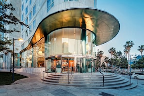 A modern hotel with a curved glass facade, a central staircase, and a sign reading 'Sorolla Palace.' - Sercotel Sorolla Palace Hotel (Valencia)
