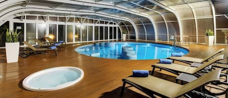 An indoor swimming pool with lounge chairs and a hot tub.