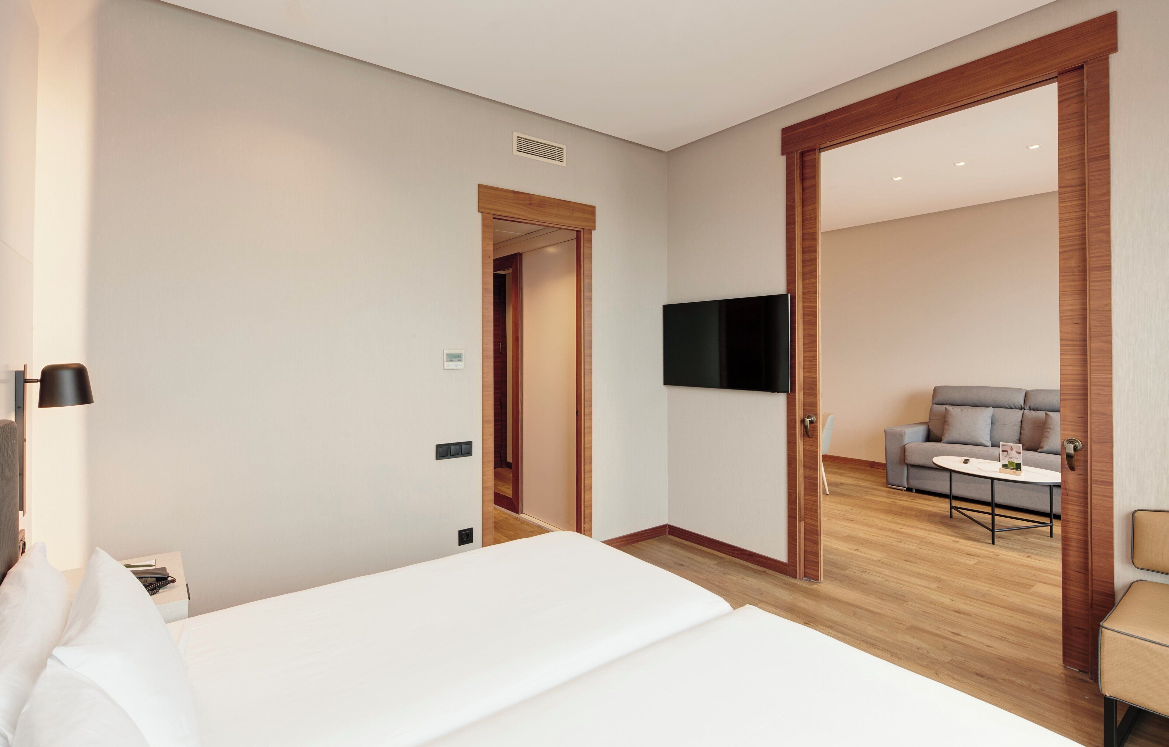 Una habitación de hotel con una cama, un televisor en la pared, un sofá y una mesita.