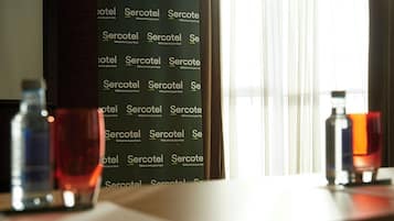Una habitación con una pared que muestra el texto repetido 'Sercotel', una ventana con cortinas translúcidas y dos botellas sobre una mesa.