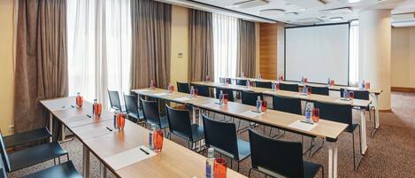 Una sala de conferencias con varias mesas, sillas y una pantalla de proyector.