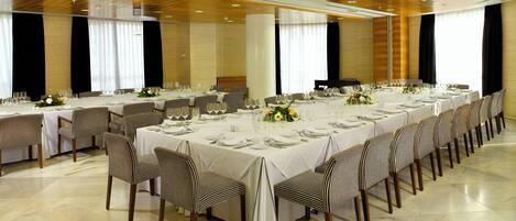 Une salle de banquet avec de longues tables dressées pour le repas, des chaises et un plancher ciré.