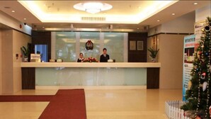 Zona de recepción de un hotel con un mostrador de cristal, dos recepcionistas, una alfombra roja y un árbol de Navidad.