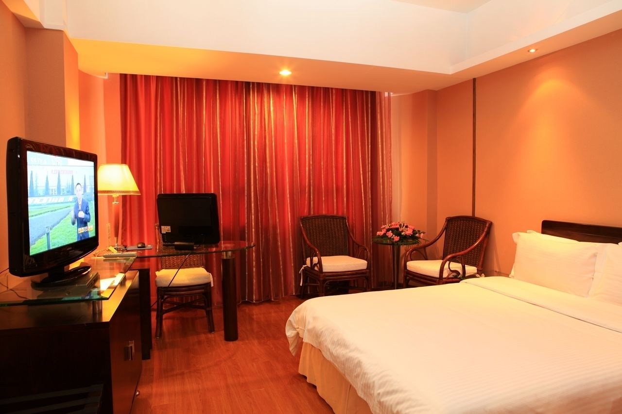Habitación de hotel con cama, escritorio con televisor, dos sillas y una mesita con flores.