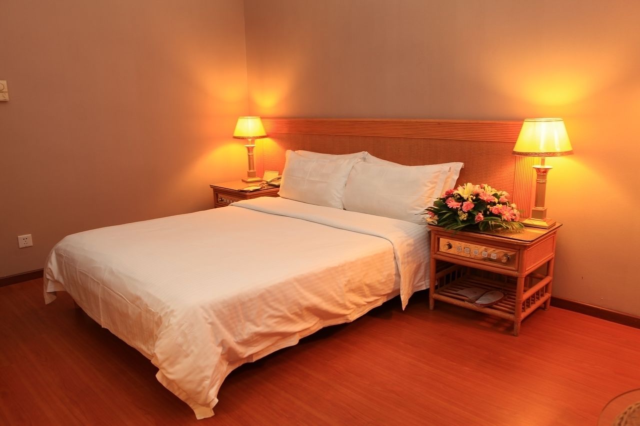 A neatly made bed with white linens, two bedside tables with lamps, and a small wooden cabinet with a flower arrangement.