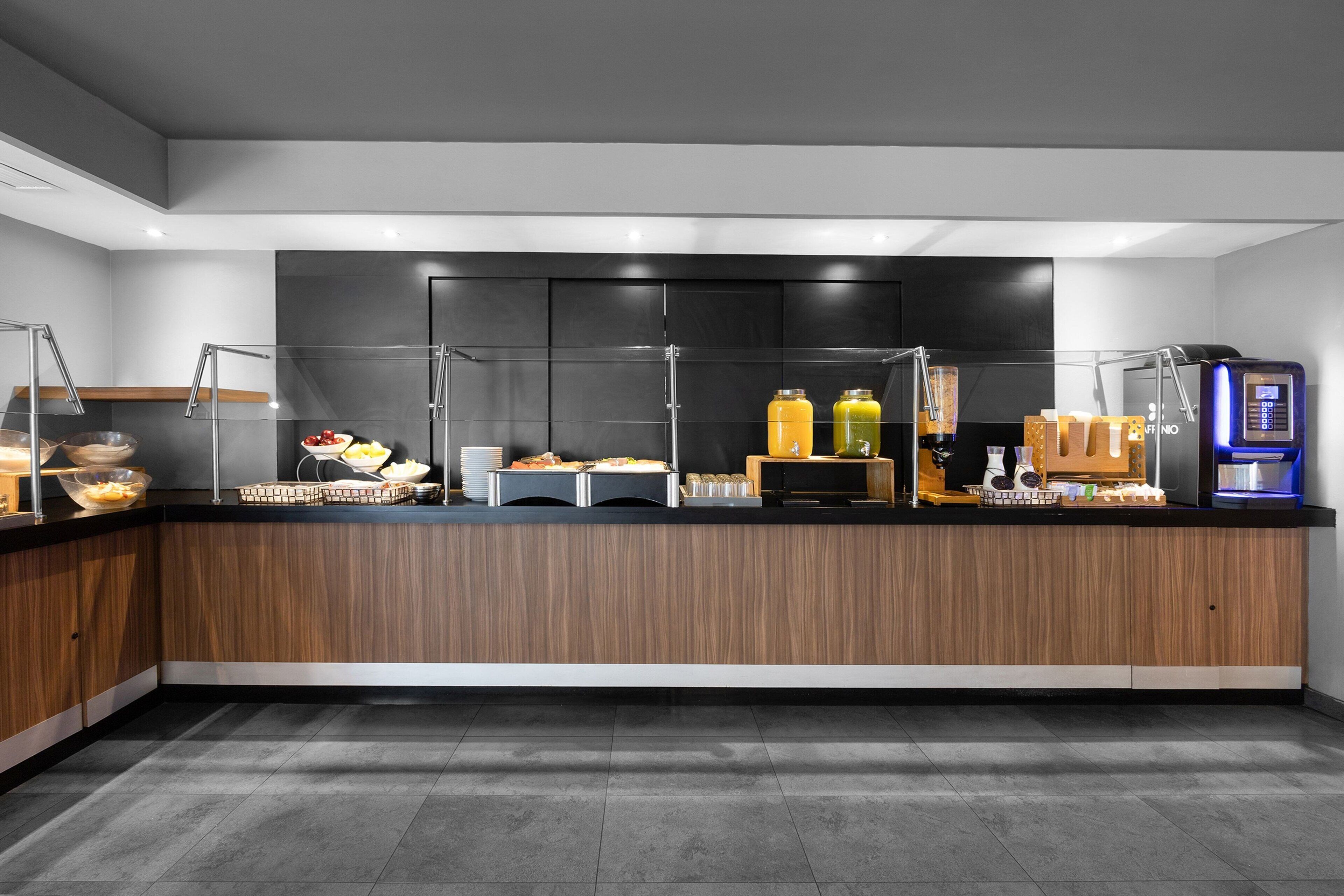 A modern breakfast bar with a variety of food and drink options, including fruits, cereals, and juice dispensers.