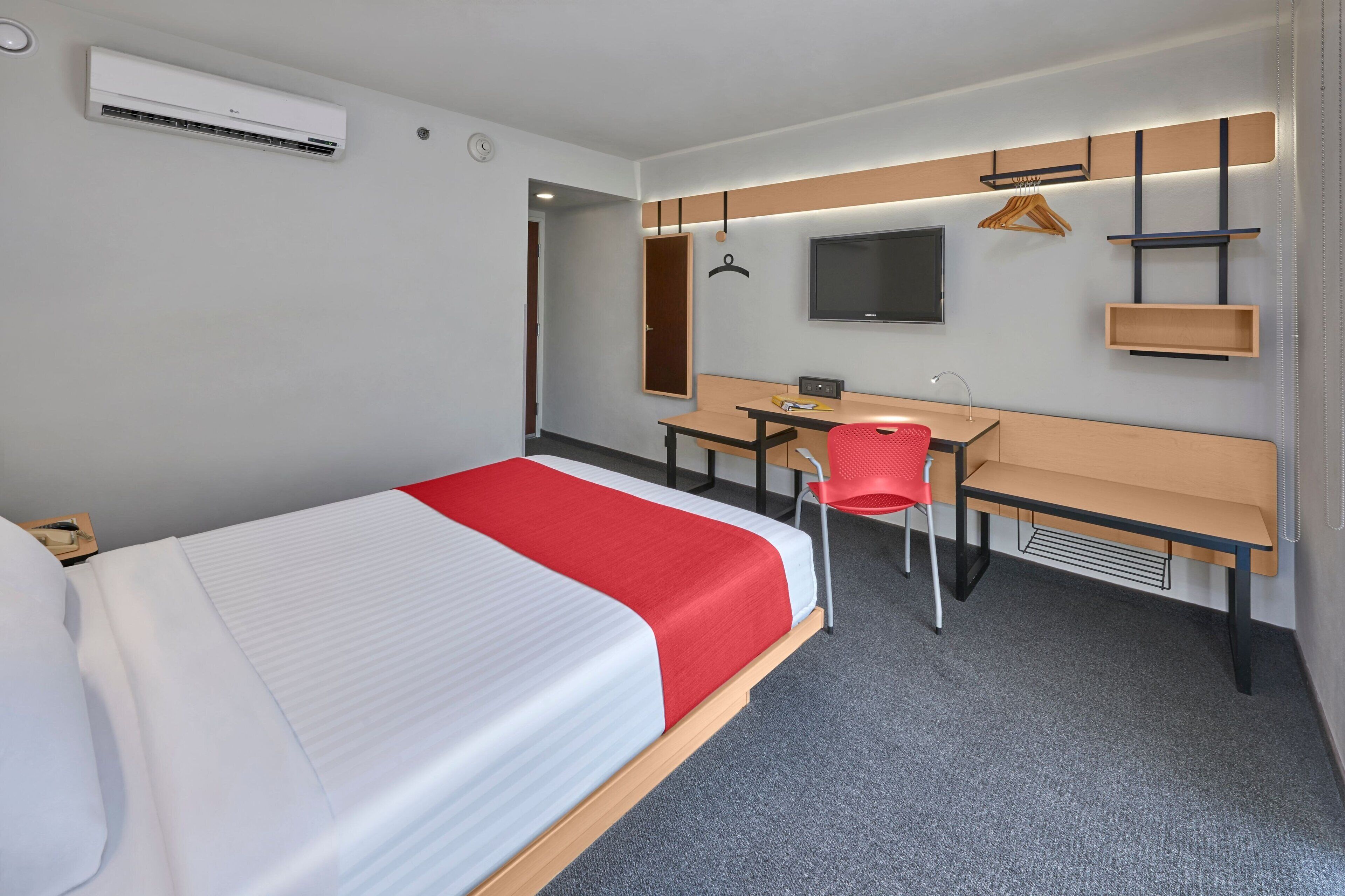A hotel room with a bed, desk, chair, TV, and built-in shelves.