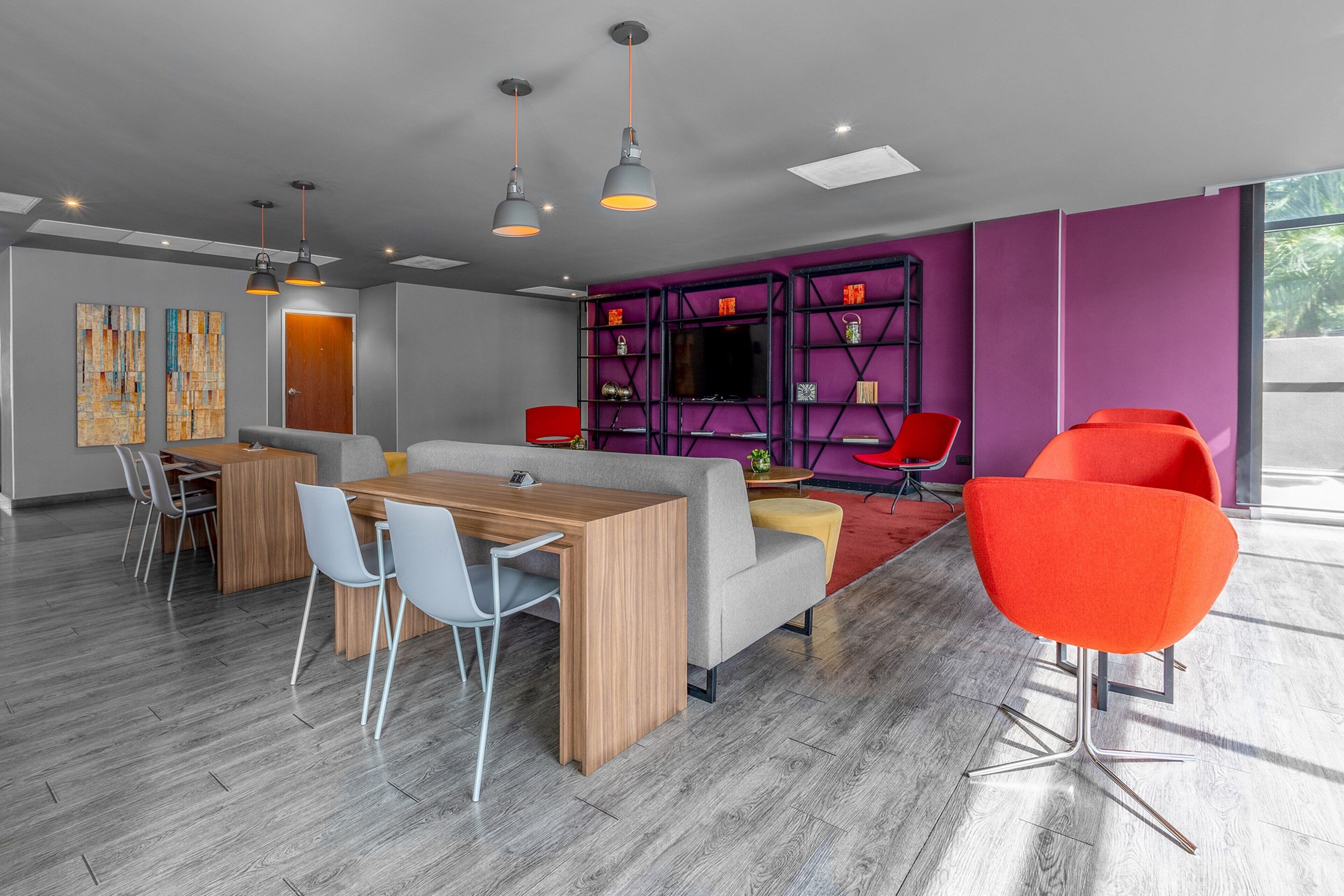 A modern office space with a wooden table and chairs, a sofa, and bright orange chairs.