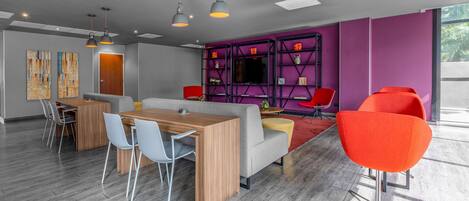 A modern office space with a wooden table and chairs, a sofa, and bright orange chairs.