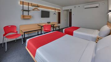 Habitación de hotel con dos camas, un escritorio, una silla, un televisor y un equipo de aire acondicionado.