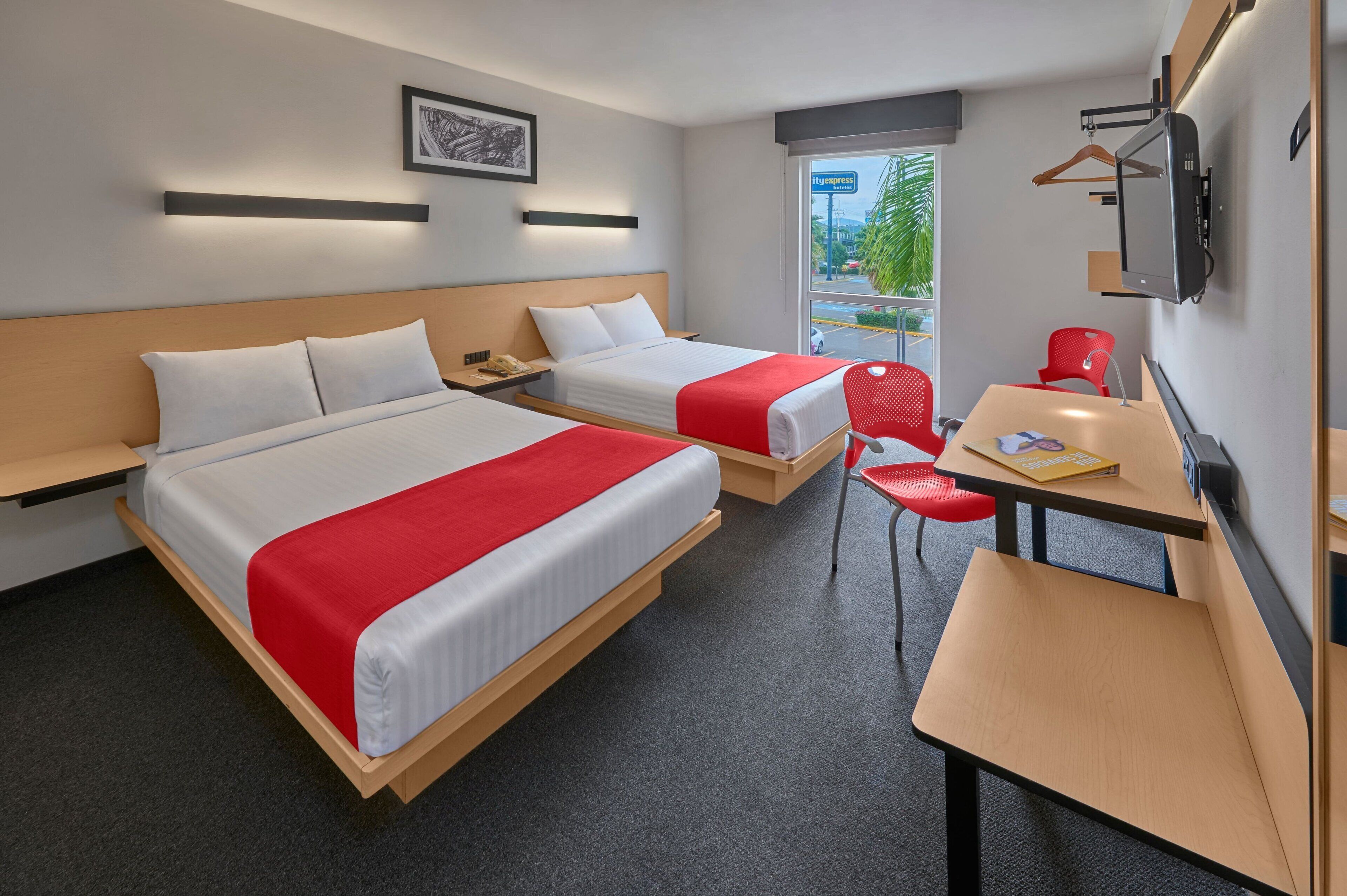 Ein Hotelzimmer mit zwei Betten, einem Schreibtisch, einem Sessel, einem Fernseher und einem Fenster mit Blick ins Freie.