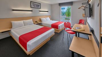 Ein Hotelzimmer mit zwei Betten, einem Schreibtisch, einem Sessel, einem Fernseher und einem Fenster mit Blick ins Freie.