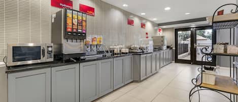 Una estación de bebidas de servicio propio con microondas, vitrina refrigerada y diversas opciones para beber.